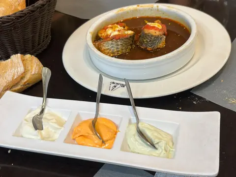 Mújol cocinado en su propio caldo con pan y una bandeja de tres salsas en El Caldero de Madrid